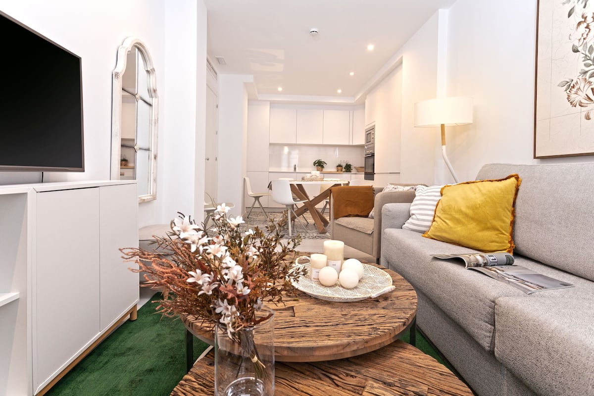 Uma sala de estar moderna com um sofá cinza, uma mesa de centro de madeira e uma TV sobre um armário branco.
