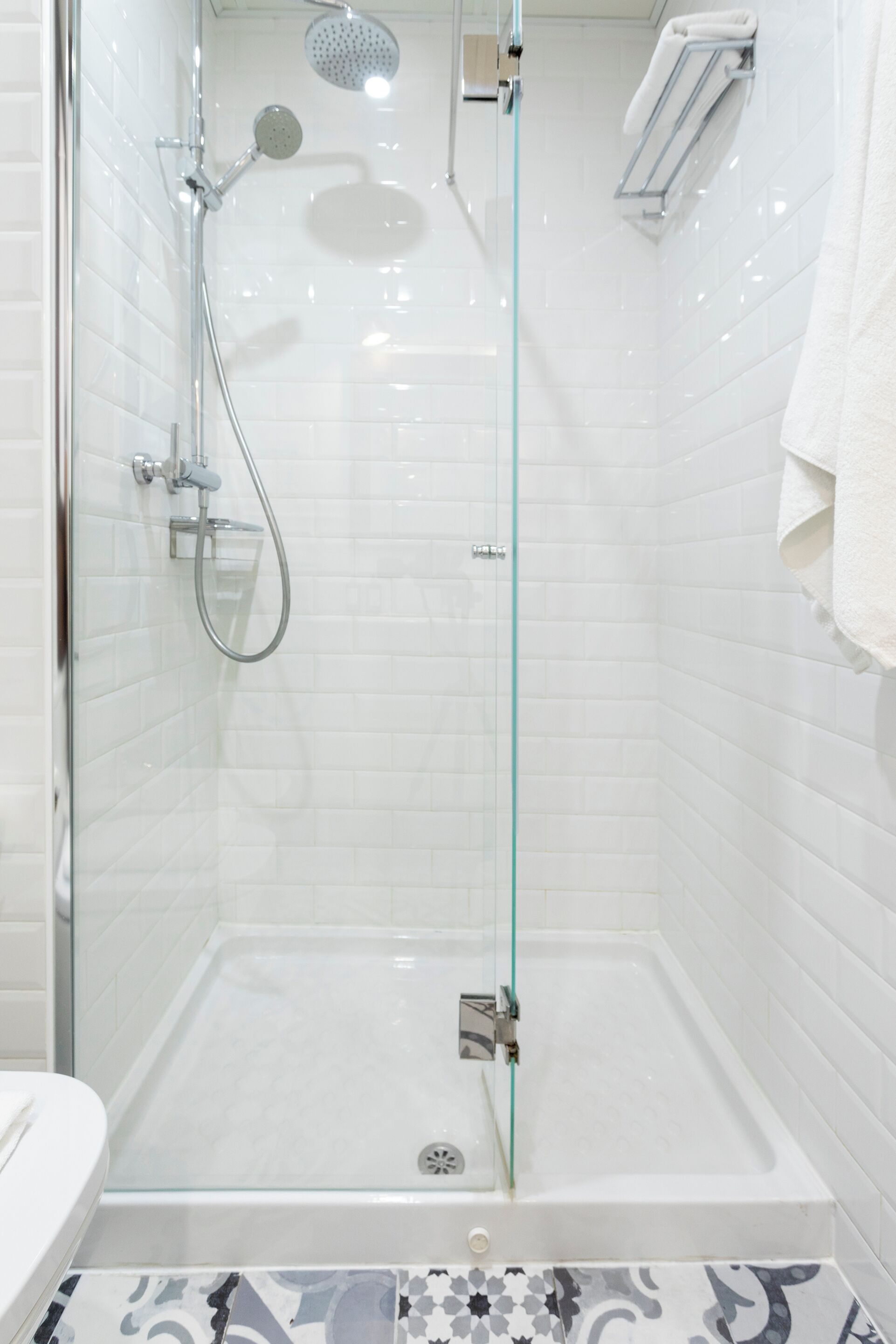 Une salle de bain moderne avec une douche à parois de verre, des murs recouverts de carreaux blancs et un sol à motifs.
