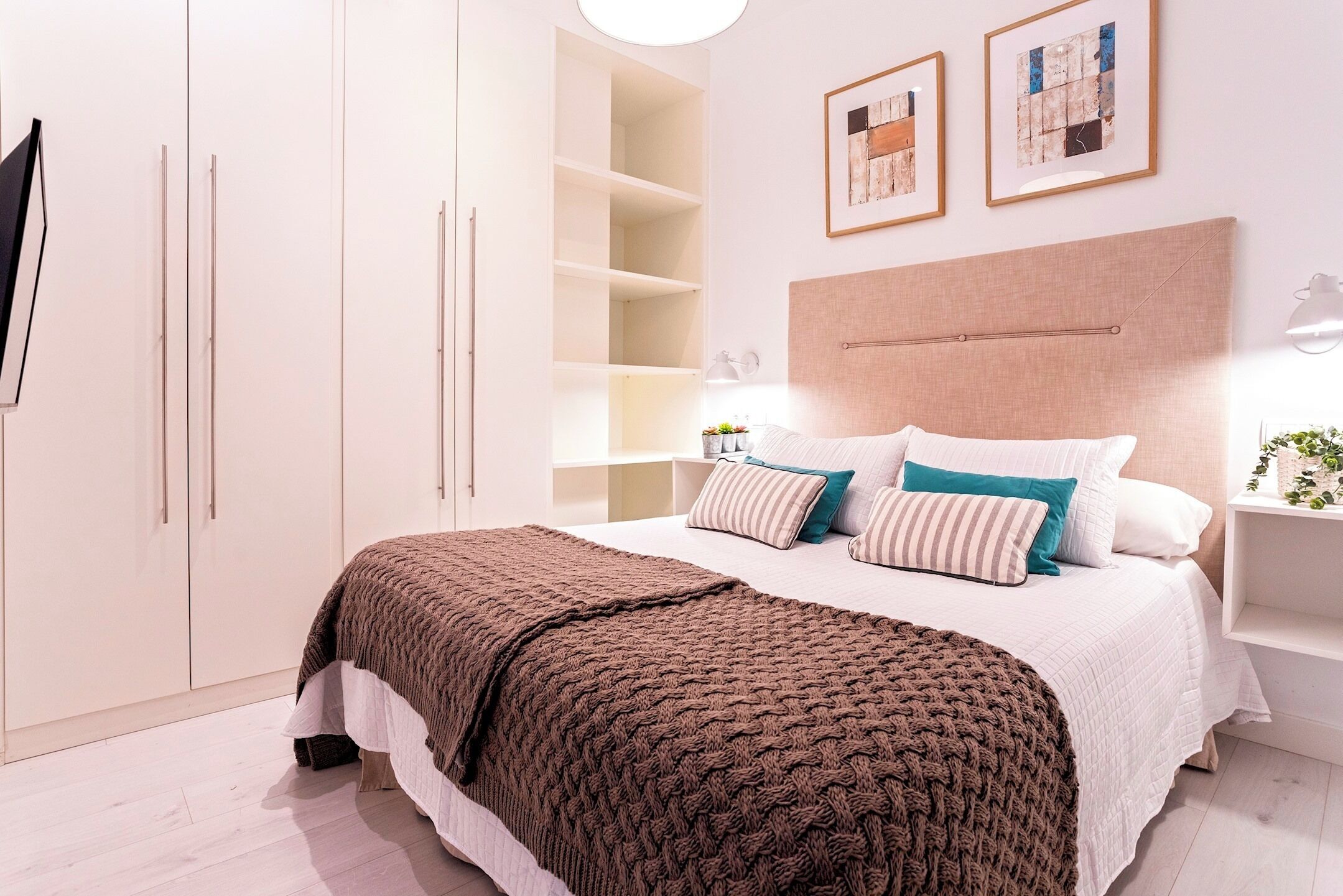 Een slaapkamer met een groot bed, een witte kast en twee kunstwerken in een lijst aan de muur.