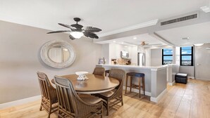 A modern kitchen with a central island, dining area with wicker chairs, and a ceiling fan.