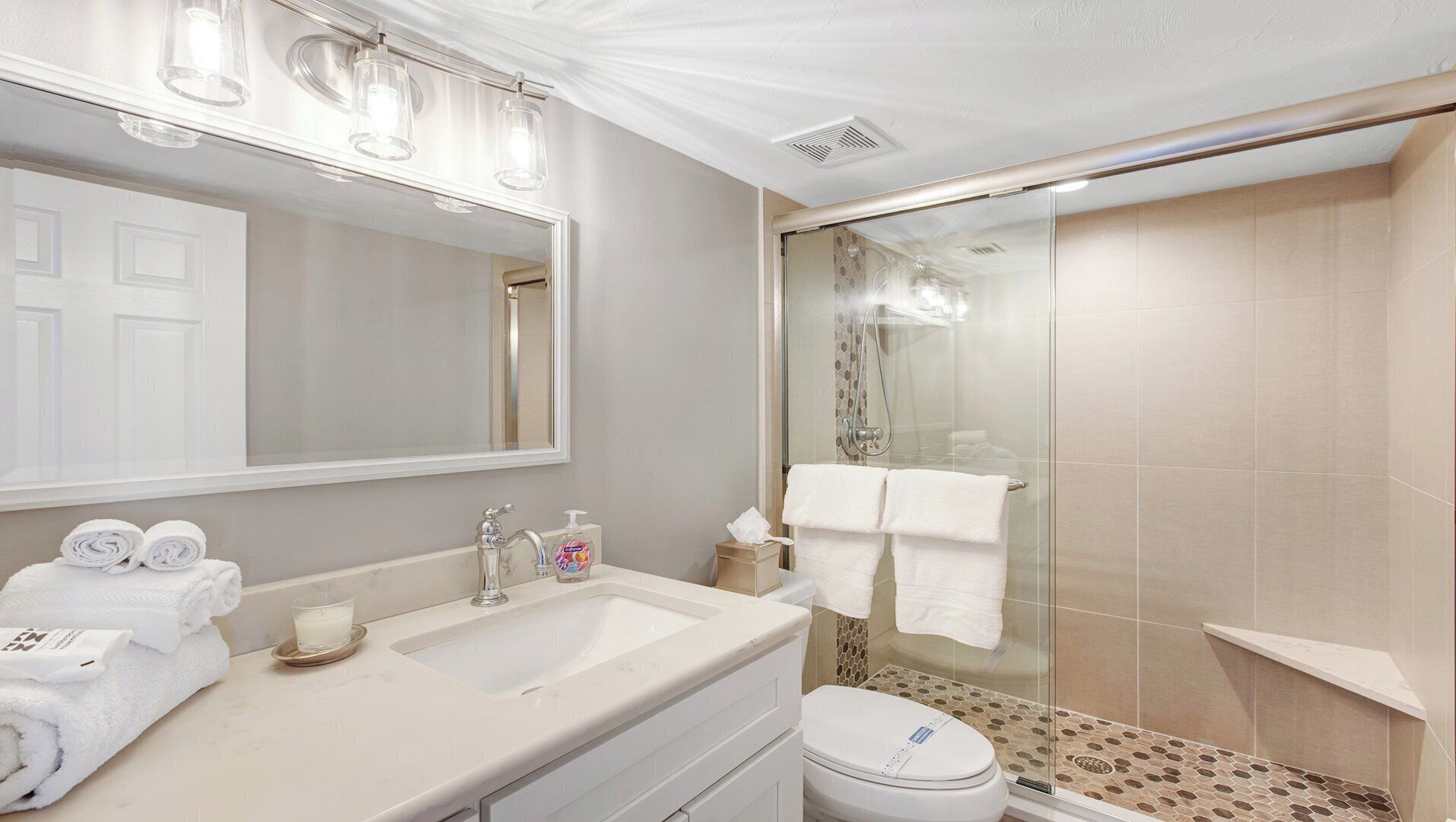 Une salle de bain moderne avec un grand miroir, deux lavabos, des toilettes et une douche à parois de verre.