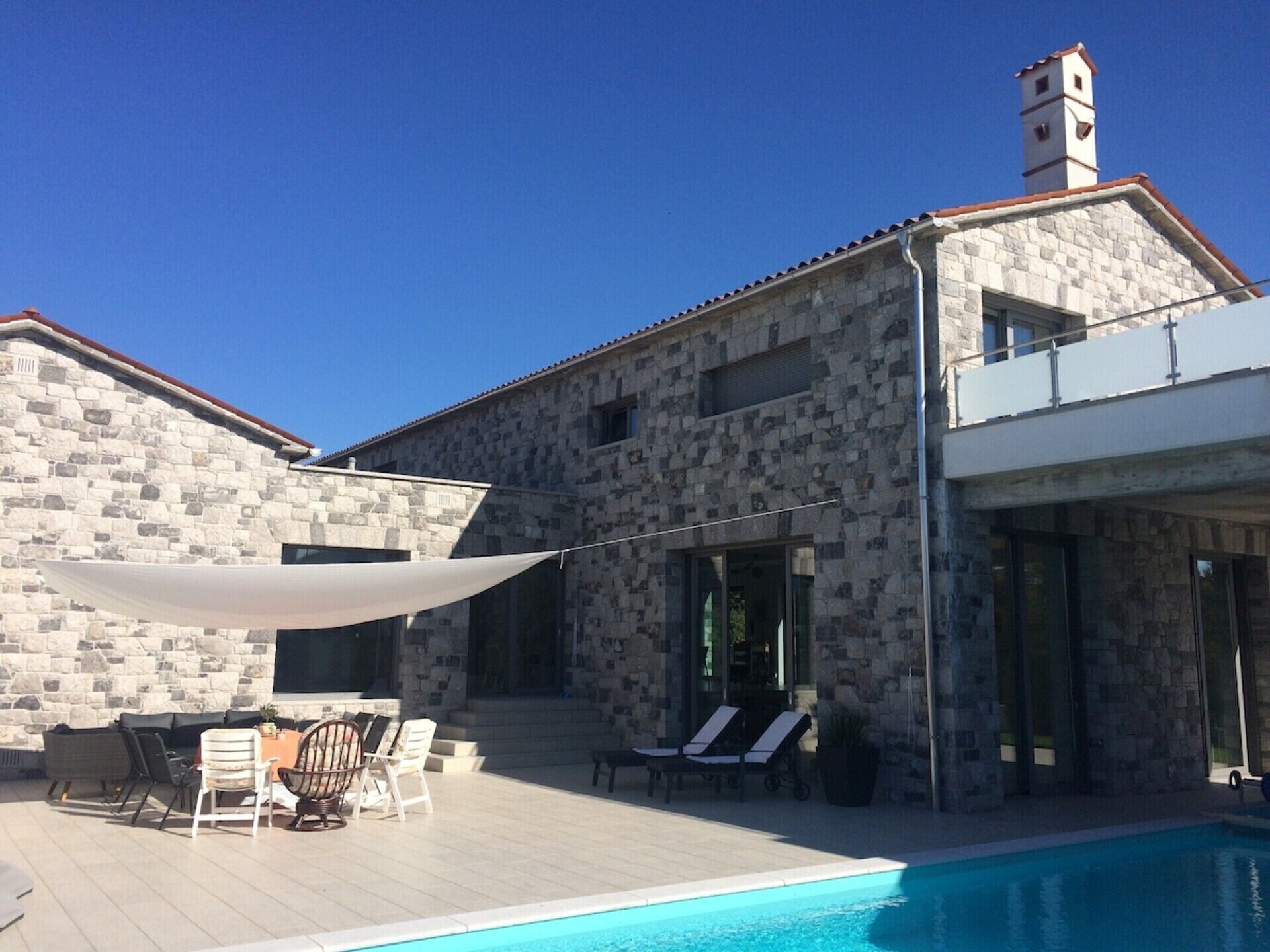 A stone building with a swimming pool, outdoor seating, and a clear blue sky.