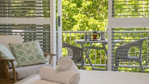 Ein Balkon mit einem Korbstuhl, einem kleinen Tisch mit einem Buch, einer Tasse und einem Topf.