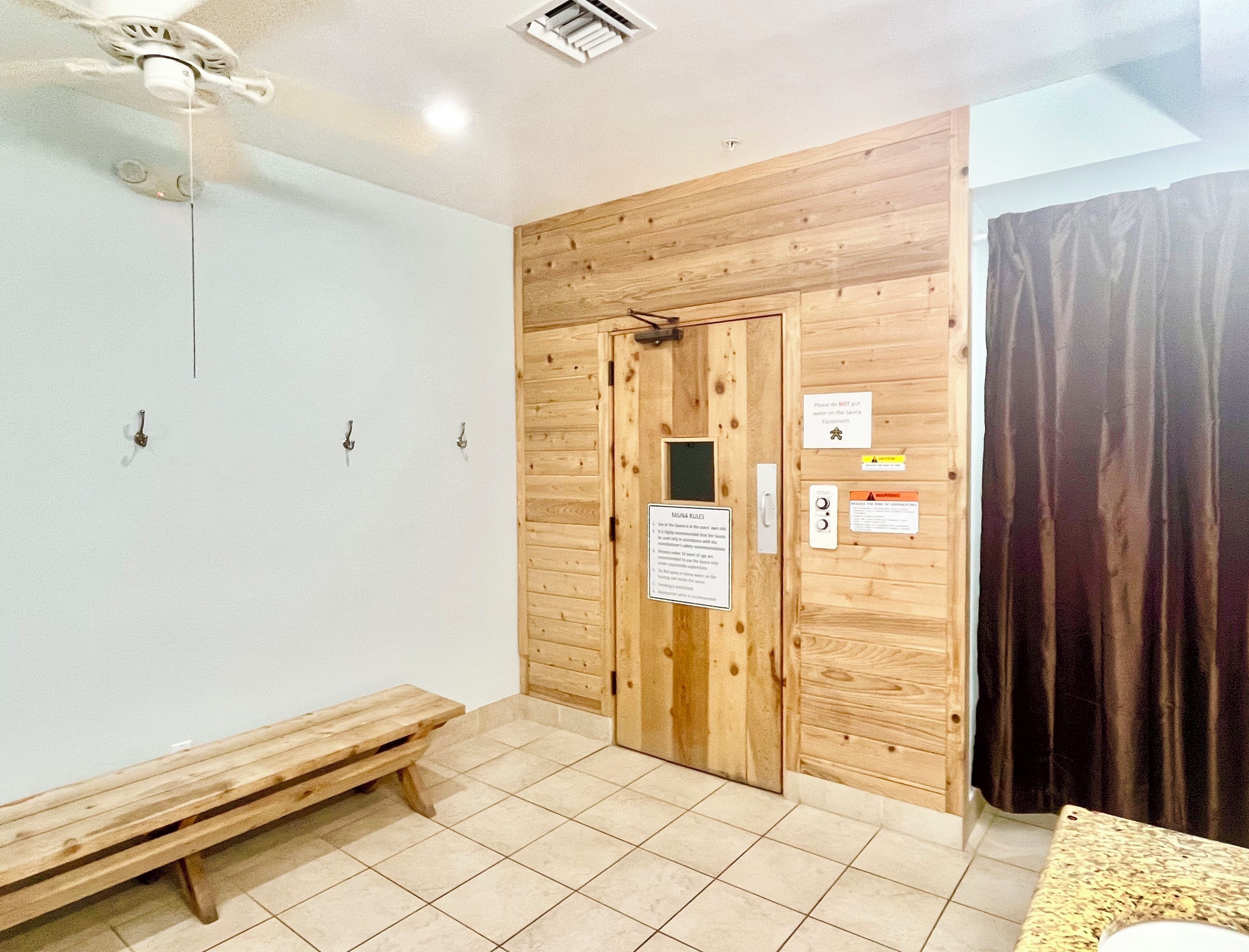 A sauna room with wooden walls, a bench, and a door. There are signs with rules and a control panel.