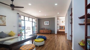 A spacious living room with a wooden floor, a glass coffee table, and colorful ottomans. - Zanzibar Beachfront Villa 1012 (Zanzibar)