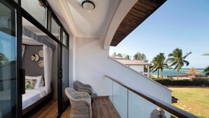 A balcony with a wooden floor, a glass door leading to a bedroom, and a view of the ocean and palm trees. - Zanzibar Beachfront Villa 1012 (Zanzibar)
