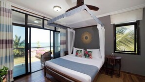 Een slaapkamer met hemelbed, uitzicht op zee en een balkon met gordijnen.