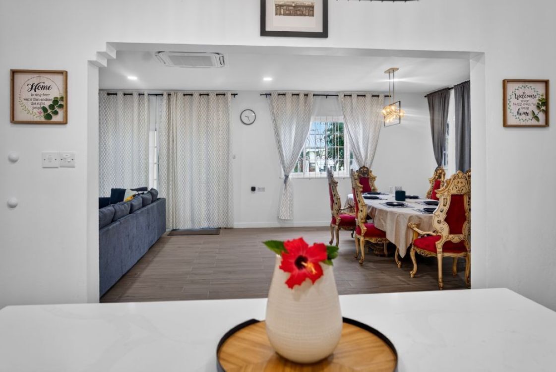 A dining area with a table set for four, a sofa, and a decorative vase with a flower.