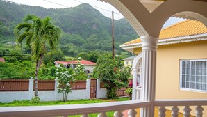 Un balcón con vistas a un paisaje verde exuberante, una palmera y una casa con techo rojo.