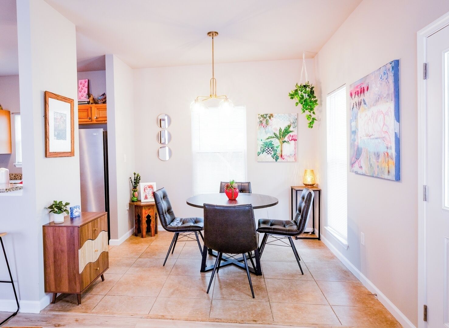 A dining area with a round table, four chairs, a hanging plant, and a painting on the wall.