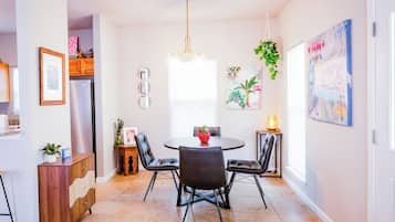 A dining area with a round table, four chairs, a hanging plant, and a painting on the wall.