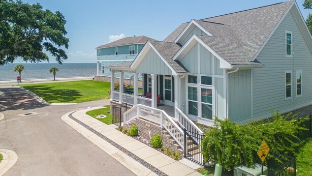 A two-story house with a covered porch, a garage, and a view of the ocean. - Coastal Comfort | 4BR Beach Retreat with Beach Views +  ShortWalk to Shore! (Pass Christian)