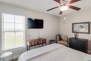 A bedroom with a bed, a TV, a ceiling fan, a desk, a chair, and a painting. - Coastal Comfort | 4BR Beach Retreat with Beach Views +  ShortWalk to Shore! (Pass Christian)