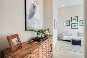 A living room with a wooden console table, a white sofa, and a coffee table. There are framed pictures on the wall and a potted plant on the table. - Coastal Comfort | 4BR Beach Retreat with Beach Views +  ShortWalk to Shore! (Pass Christian)