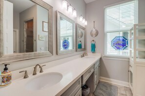 Un baño con un tocador amplio, dos espejos, un lavabo y una ventana con persianas.