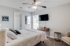 Un dormitorio con cama, ventilador de techo, televisor, cómoda y una silla.