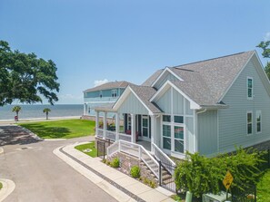 A two-story house with a covered porch, a garage, and a view of the ocean. - Coastal Comfort | 4BR Beach Retreat with Beach Views +  ShortWalk to Shore! (Pass Christian)