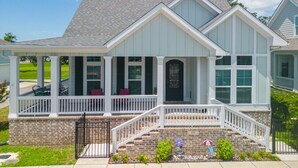 A two-story house with a covered porch, a brick foundation, and a front door with a decorative window above it. - Coastal Comfort | 4BR Beach Retreat with Beach Views +  ShortWalk to Shore! (Pass Christian)