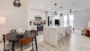 Una cocina moderna con una isla central, armarios blancos, electrodomésticos de acero inoxidable e iluminación colgante.