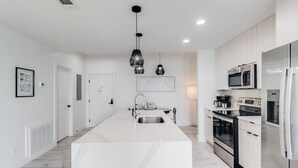 Una cocina moderna con armarios blancos, electrodomésticos de acero inoxidable e iluminación colgante.