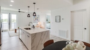 Una cocina moderna con una isla de mármol, luces colgantes y un comedor con mesa y sillas.