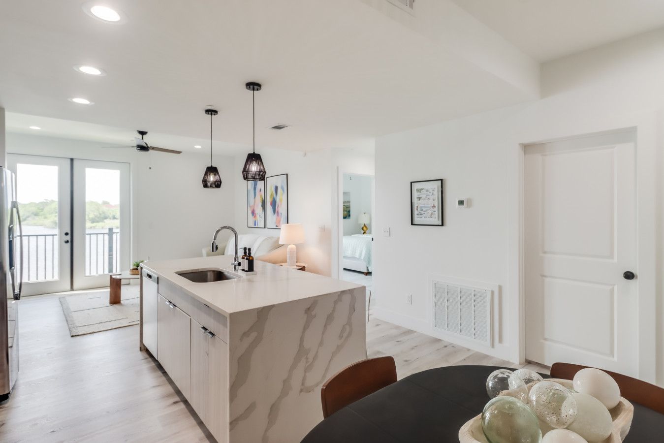 A modern kitchen with a marble island, pendant lights, and a dining area with a table and chairs.