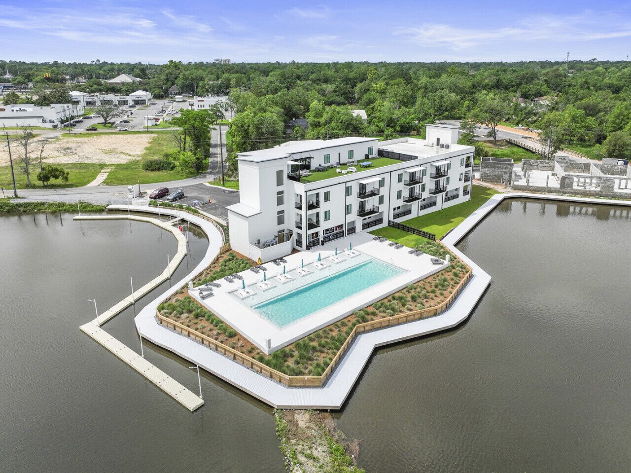 A modern hotel with a pool, surrounded by water and greenery.