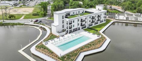 A modern hotel with a pool, surrounded by water and greenery.