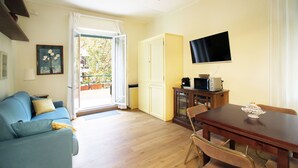 Una sala de estar con sofá, mesa de comedor, televisor montado en la pared y vistas a través de un ventanal.