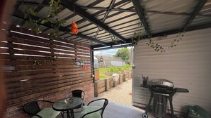 An outdoor patio area with a table and chairs, a grill, and a wooden fence.
