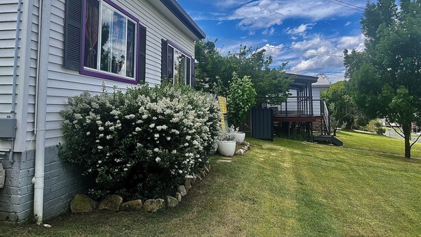 A house with a well-maintained lawn, a large flowering bush, and a deck.