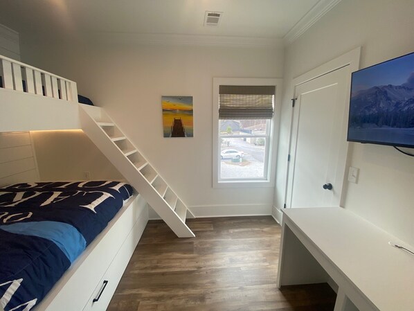 A bedroom with a bunk bed, a desk, a chair, a window with blinds, and a painting on the wall. - Splash at Lake Martin (Alexander City)