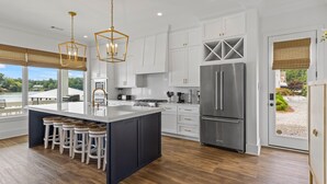 Une cuisine moderne dotée d’un grand îlot central, de meubles blancs, d’appareils électroménagers en acier inoxydable et offrant une vue sur l’extérieur.