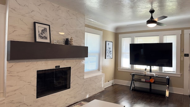 A living room with a fireplace, a mounted TV, and a ceiling fan.