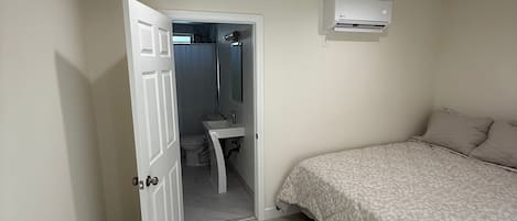 A bedroom with a bed, a door leading to a bathroom, and an air conditioning unit on the wall.