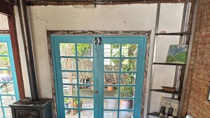Ein gemütliches Zimmer mit Holzboden, einem weißen Sofa, einem Tisch mit zwei weißen Tassen und einer blauen Tür mit Blick zum Garten.