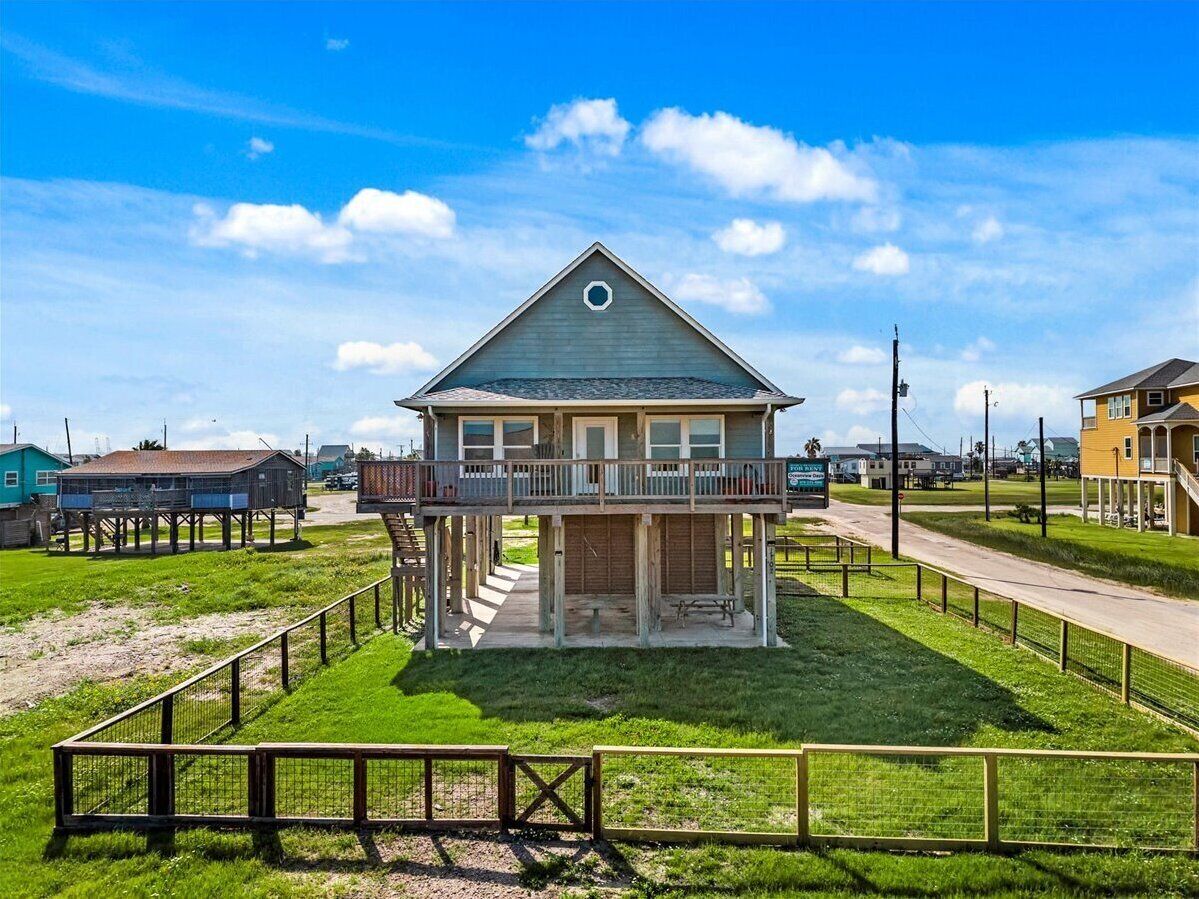 A two-story house with a balcony, surrounded by a wooden fence, and located near a road.