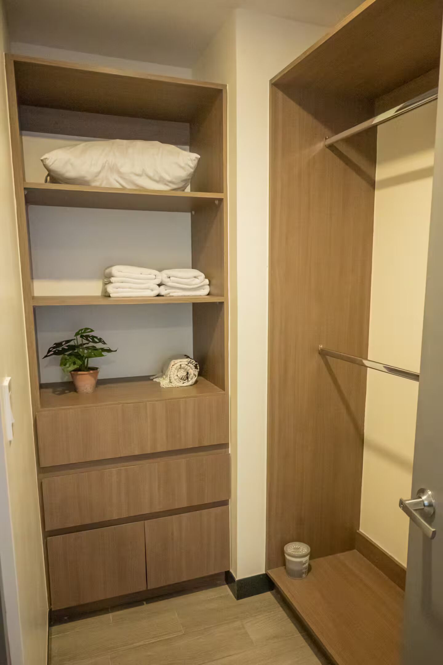 Een houten kast met planken waar gevouwen handdoeken, een potplant en een decoratief object op staan.