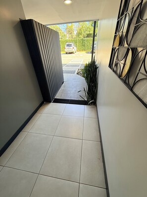 Ein Korridor mit Fliesenboden, einem Metallgitter und einer Wand mit geometrischem Muster.