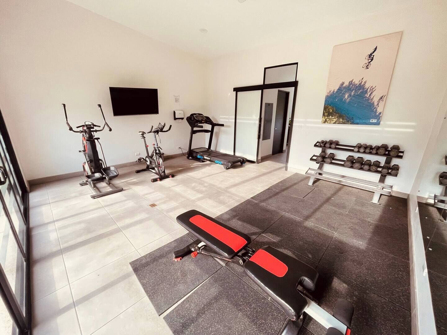 A home gym with exercise equipment including a treadmill, stationary bikes, and a bench press.