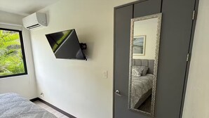 A bedroom with a bed, a TV mounted on the wall, a wardrobe, and a mirror reflecting the room. - 5 minutes from Airport | Transfer ($) | Pool | Gym | Full condo (Provincia de Alajuela)