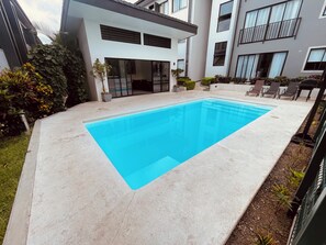 Ein modernes Wohngebäude mit einem rechteckigen Schwimmbad, umgeben von einem gepflegten Garten und einer Sitzgelegenheit im Freien.