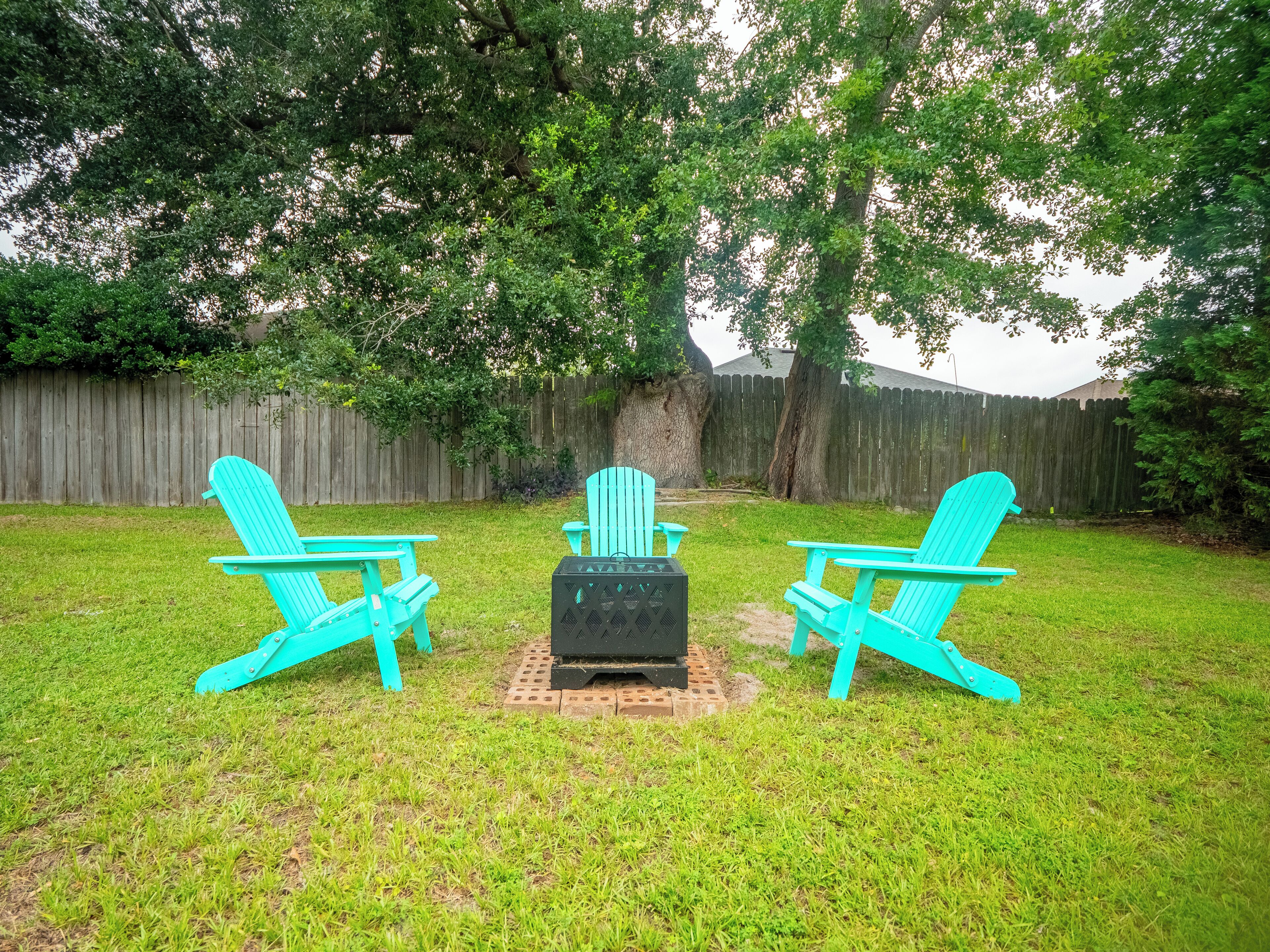 A backyard with three turquoise Adirondack chairs arranged around a black grill.