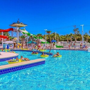 A swimming pool with multiple lanes, a water slide, and a covered area with palm trees. - NEWLY Furnished 6BR, Lake Views, Steps to Beach, Pool & Amenities (Myrtle Beach)