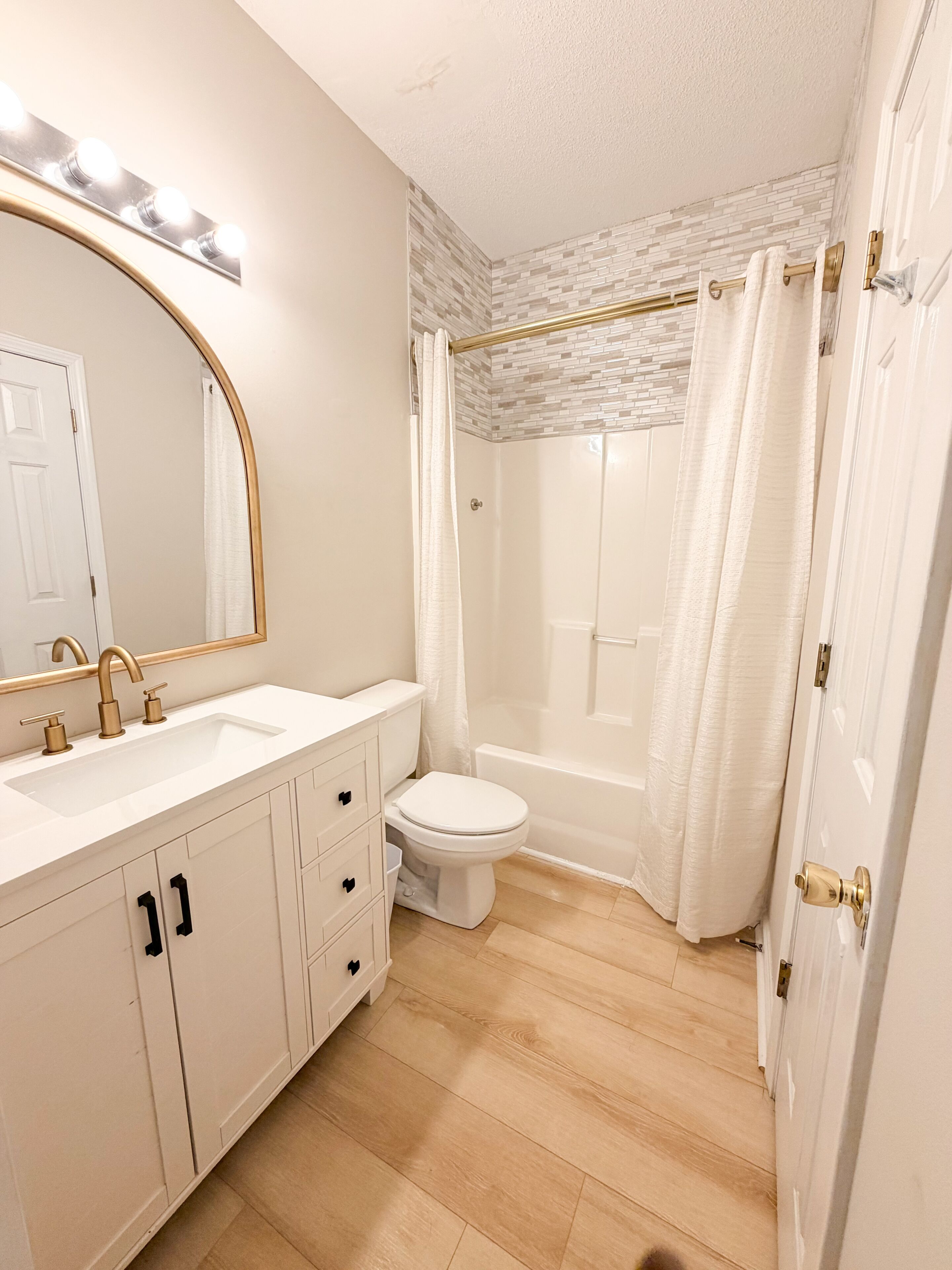 Une salle de bain avec un lavabo, un meuble-lavabo et des toilettes, tous de couleur blanche. Elle est équipée d’une douche avec une porte en verre et d’un espace de douche carrelé.