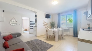 Una sala de estar moderna con un sofá gris, una mesa de comedor con sillas, una zona de cocina y un ventanal con cortinas.