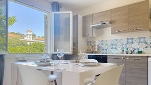 Una cocina moderna con armarios blancos, una mesa de comedor con sillas y vistas a un edificio por la ventana.