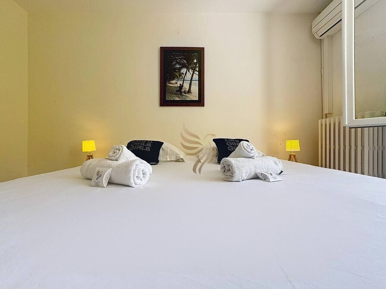 A hotel room with a large bed, two pillows, a framed picture on the wall, and two bedside lamps.