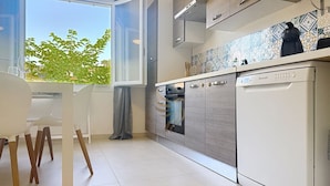 Una cocina moderna con horno integrado, lavavajillas y ventana con vista a árboles.