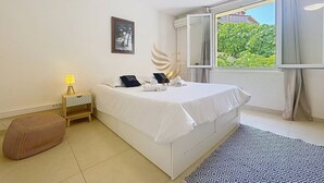 Un dormitorio con cama, mesita de noche, lámpara y ventana con vistas a zonas verdes.